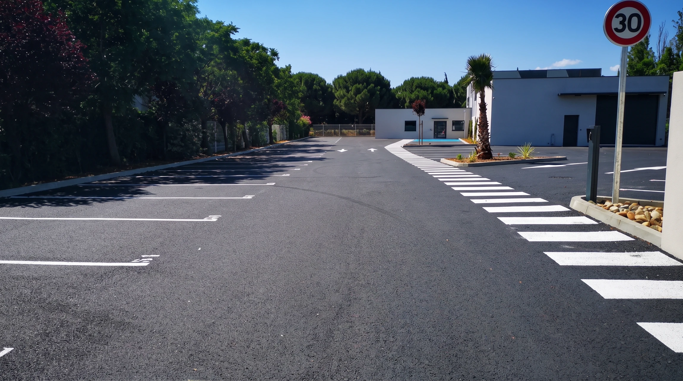 Parking neuf avec marquage au sol blanc fraîchement peint : places de stationnement, flèches directionnelles et passage piéton zébré