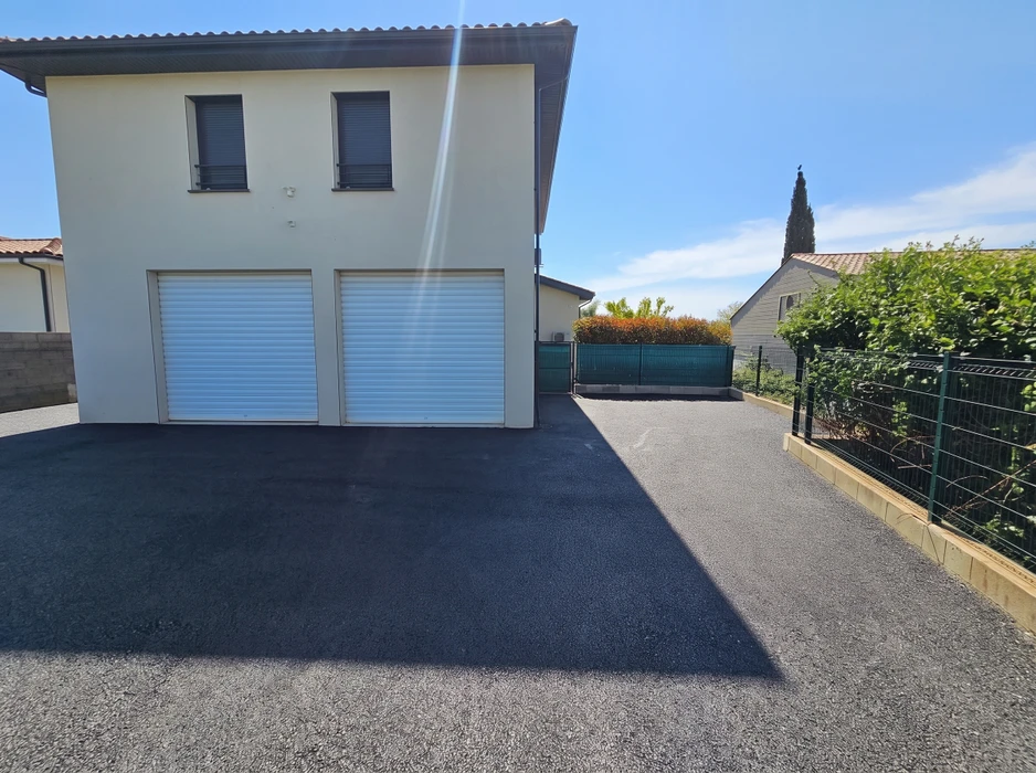 Allée de maison pavée en enrobé bitumineux noir, devant un double garage à portes à enroulement blanches