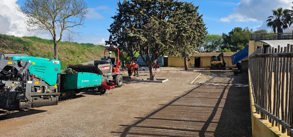 Chantier de voirie extérieur, équipe de deux ouvriers en EPI orange travaillant sur une aire en cours d'enrobé