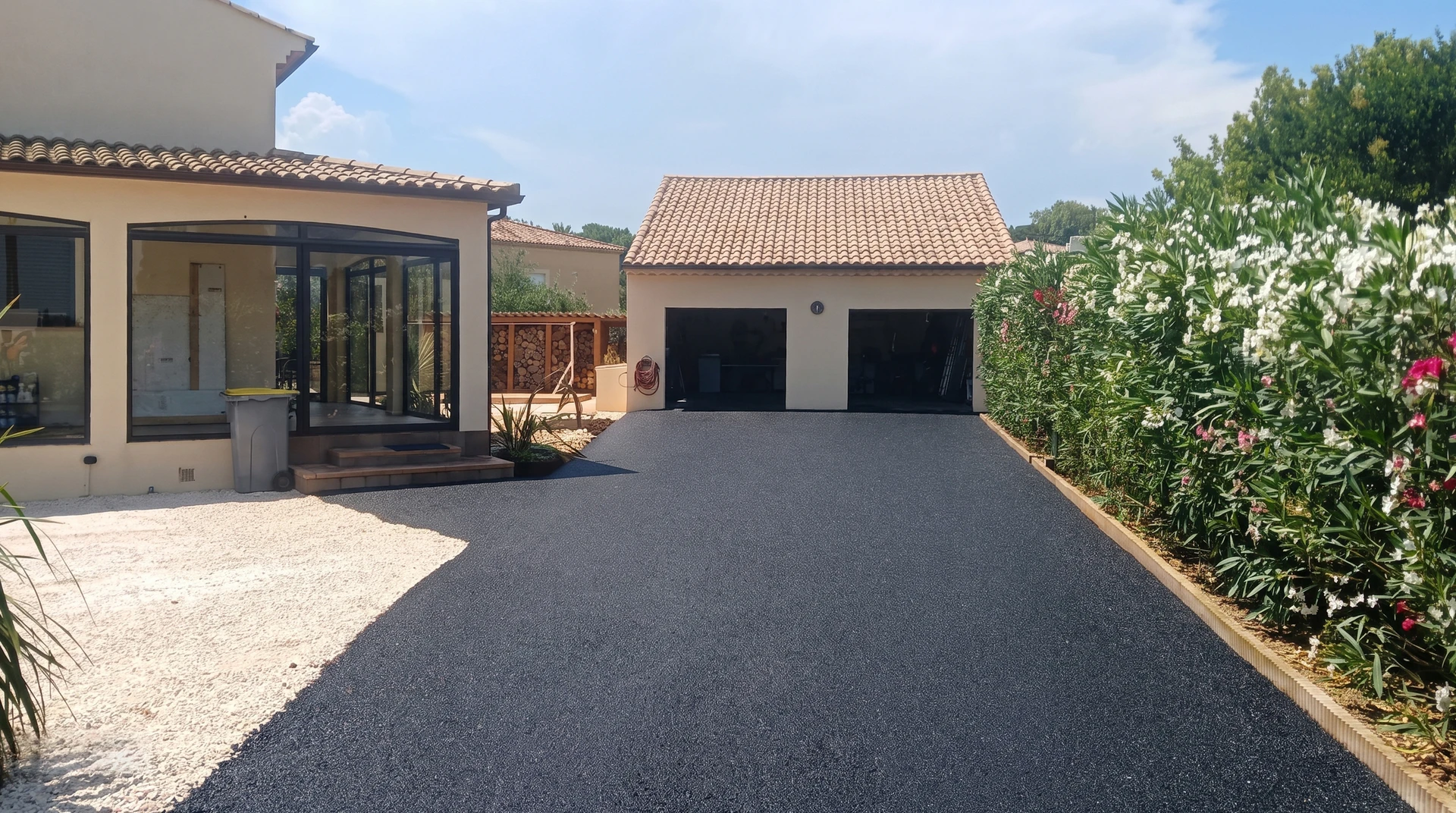 Allée privée en enrobé bitumineux noir fraîchement posé, menant à un garage double attenant